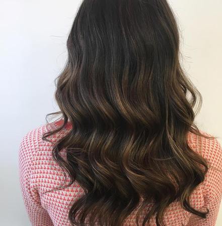 Frau mit langen, glänzenden braunen Haaren und sanften Wellen vor hellem Hintergrund.