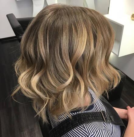 Blonde Balayage Frisur mit sanften Wellen im modernen Friseursalon gestylt.