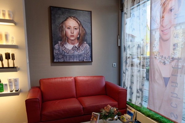 Moderner Friseursalon mit rotem Ledersofa, Wandbild und Pflegeprodukten im Wartebereich.